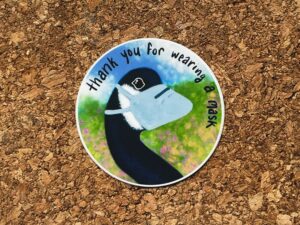 Nikki's "Thank You For Wearing a Mask" sticker displayed on a cork background.