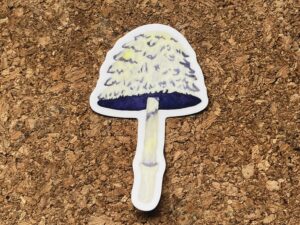 Nikki's "Autumnal Equinox Mushroom" sticker displayed on a cork background.