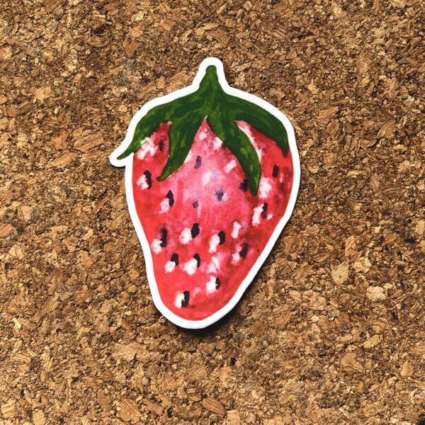 Nikki's "Summer Solstice Strawberry" sticker displayed on a cork background.