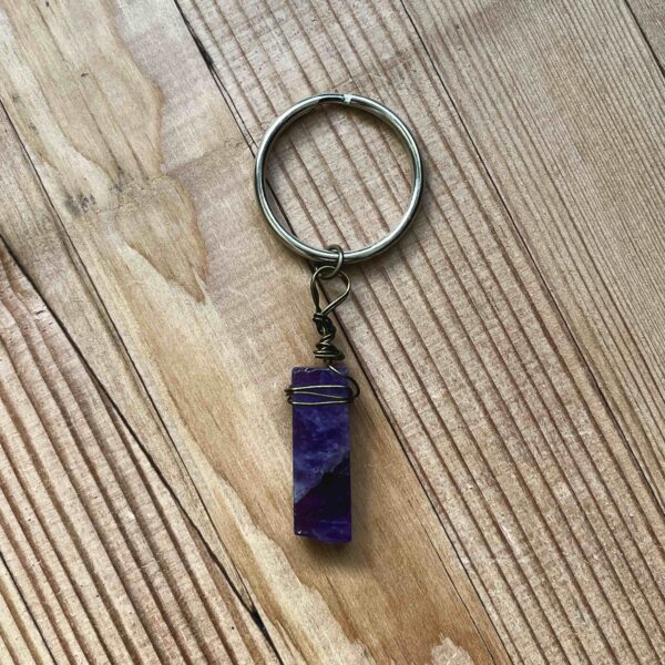 One of Nikki's keychain designs. A rectangular prism shaped amethyst crystal is wrapped with wire and attached to a silver split ring (keychain ring).