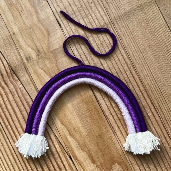 One of Nikki's mini rainbows. The rainbow is made of cotton thread, rope, and wire; and has a string to hang it from. The rainbow has three colours (listed from the outer arch to the inner one): dark purple, medium purple, light purple.