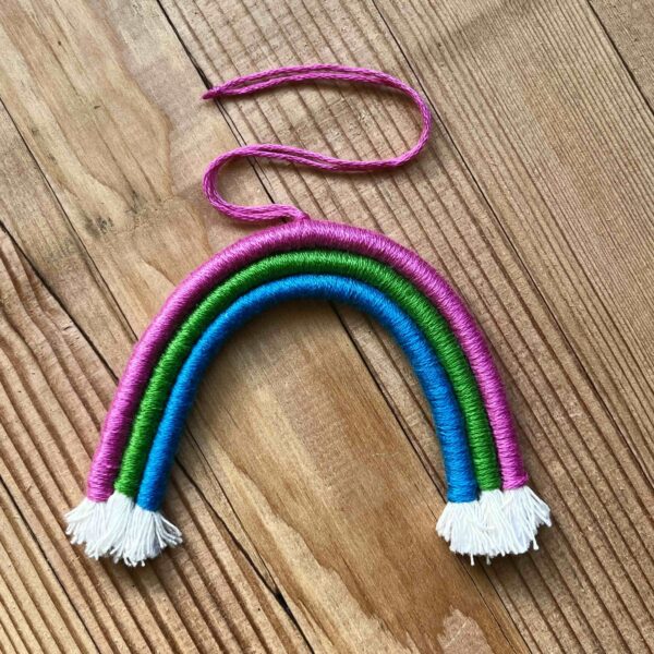 One of Nikki's mini rainbows. The rainbow is made of cotton thread, rope, and wire; and has a string to hang it from. The rainbow has three colours (listed from the outer arch to the inner one): hot pink, bright green, sky blue.