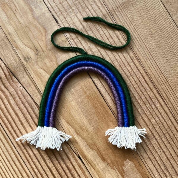 One of Nikki's mini rainbows. The rainbow is made of cotton thread, rope, and wire; and has a string to hang it from. The rainbow has three colours (listed from the outer arch to the inner one): dark green, dark blue, dark purple.