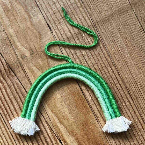 One of Nikki's mini rainbows. The rainbow is made of cotton thread, rope, and wire; and has a string to hang it from. The rainbow has three colours (listed from the outer arch to the inner one): dark green, medium green, light green.