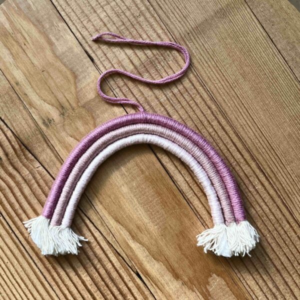 One of Nikki's mini rainbows. The rainbow is made of cotton thread, rope, and wire; and has a string to hang it from. The rainbow has three colours (listed from the outer arch to the inner one): dark pink, medium pink, light pink.
