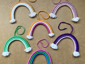 6 mini rainbows arranged on a light brown background. The rainbows are made of cotton thread, rope, and wire; and all feature a string to hang them from.