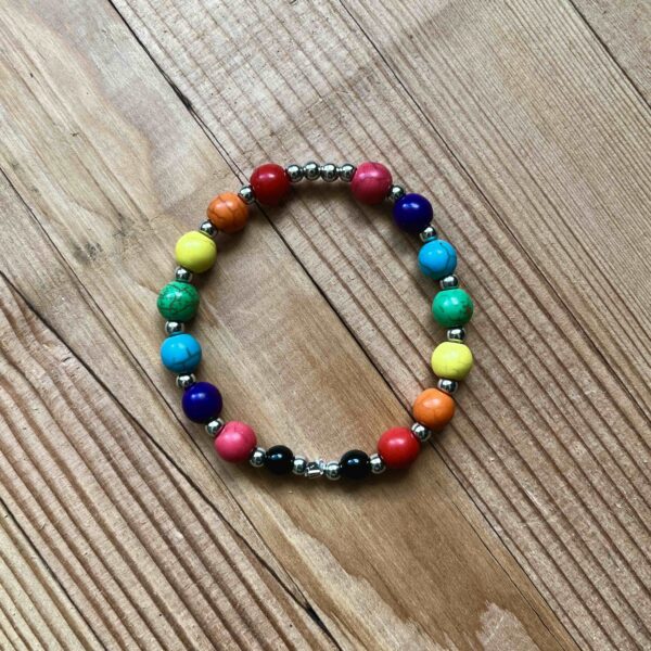 Nikki's Pride bracelet. It has two sets of rainbow beads (red, orange, yellow, green, blue, purple, pink) with a smaller silver bead between each of the coloured ones. There are two small black beads near where the two ends of the bracelet come together.